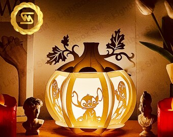 May include: A white pumpkin-shaped lamp with a light inside. The lamp has a design of a cartoon character on the front. The lamp is sitting on a table with a book and other decorative items.