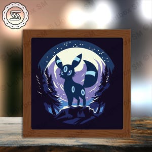 Op de afbeelding: Een ingelijste kunstdruk met een donkerblauwe Umbreon-personage uit de Pokémon-serie, tegen een maanverlichte bosscène. Het kunstwerk bevindt zich in een vierkante houten lijst, met een volle maan en sterrenhemel op de achtergrond.