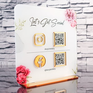 May include: White acrylic sign with the text "Let's Get Social" and gold icons for Instagram, Facebook, and two QR codes. The sign has a gold stand and floral accents.