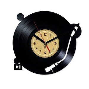 Puede incluir: Un reloj de vinilo negro con una esfera blanca y agujas negras. El reloj tiene forma de tocadiscos con un brazo de lectura y un disco en el plato giratorio. La esfera del reloj tiene números negros y un fondo blanco.
