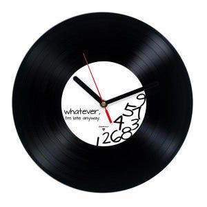 May include: A black vinyl record clock with a white center. The clock hands are black with a red second hand. The numbers are partially visible, and the text "whatever, I'm late anyway." is printed on the clock face.