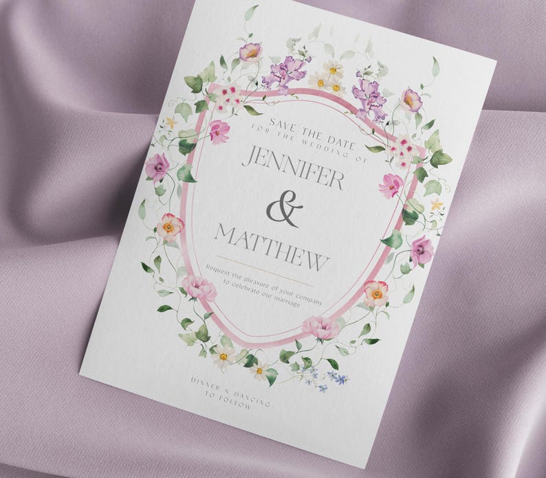 Op de afbeelding: Een trouwkaart met een bloemenontwerp. De uitnodiging heeft een roze en wit schildvormig frame met de namen "Jennifer & Matthew" in het midden. De tekst "Save the Date" en "Dinner & Dancing to Follow" zijn ook zichtbaar.