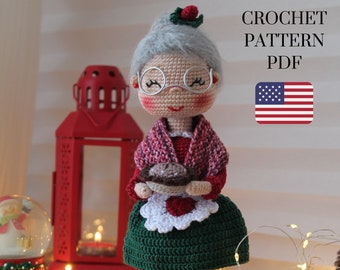 May include: Crochet pattern PDF for a granny doll holding a pie. The doll is wearing a green dress, a red sweater, and a white apron. The doll has gray hair, glasses, and rosy cheeks.