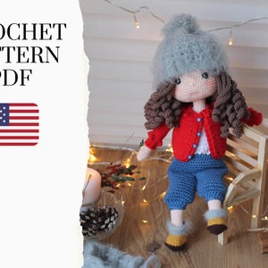 May include: Crochet pattern PDF for a doll wearing a red cardigan, blue jeans, and a gray hat. The doll is sitting on a wooden bench. The image also includes a US flag.