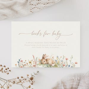 Op de afbeelding: Een uitnodiging voor een babyshower met de tekst "books for baby" in een sierlijk handschrift. De kaart toont een aquarel illustratie van een konijn tussen wilde bloemen, met extra tekst.