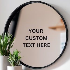 以下が含まれることがあります： 黒いフレームの丸い鏡。鏡には「YOUR CUSTOM TEXT HERE」と書かれたステッカーが貼られています。