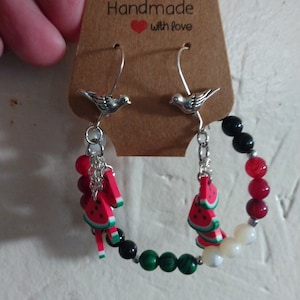 May include: A pair of handmade earrings featuring watermelon slices, black and green beads, and silver bird charms. The earrings are labeled "Handmade with love".