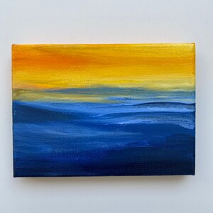Puede incluir: Pintura abstracta sobre lienzo con una división horizontal de colores. La mitad superior es de un amarillo vibrante con matices anaranjados, mientras que la mitad inferior es de un azul profundo con sutiles pinceladas de azul más claro.