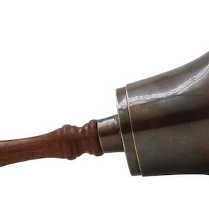 Pu&ograve; includere: Una campana color bronzo con manico in legno. La campana ha una forma svasata e una superficie liscia e lucida. Il manico &egrave; di colore marrone scuro e ha una forma arrotondata con una piccola sfera all'estremit&agrave;. La campana viene probabilmente utilizzata per segnalare.