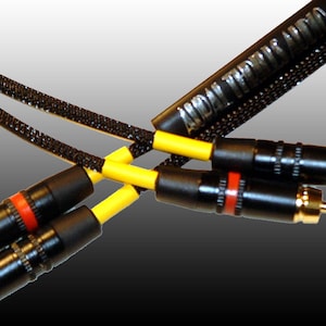 Puede incluir: Primer plano de dos cables de audio RCA negros con detalles amarillos y rojos. Los cables están conectados a conectores RCA chapados en oro.
