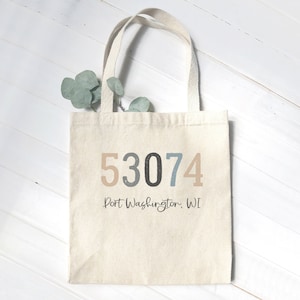 May include: A beige canvas tote bag with a zip code "53074" and the text "Port Washington, WI" printed on the front.