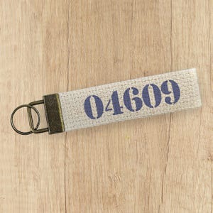 May include: A beige fabric keychain with a metal ring and a blue number "04609" printed on it.