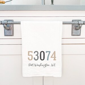May include: White kitchen towel with the text "53074 Port Washington, WI" printed in brown, gray, and black.