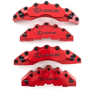 Puede incluir: Un juego de cuatro cubiertas para pinzas de freno de color rojo brillante, cada una con el logotipo y el texto de Lexus en negro. Estos componentes automotrices tienen un acabado metálico liso con pernos negros visibles y clips laterales.