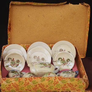 May include: A vintage miniature tea set in a decorative box. The set includes small white plates, saucers, cups, and a teapot, all with hand-painted designs in red, green, and brown. The box is lined with pink paper and has a floral pattern.