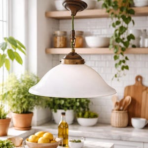 May include: A white glass pendant light with a brass and bronze fixture hangs in a kitchen. The light is suspended from a green cord. The kitchen features wooden shelves, plants, and a marble countertop.