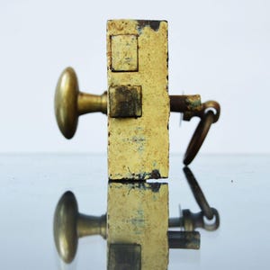 May include: A vintage brass door lock with a key and a round knob. The lock is painted yellow and has a worn, aged look.
