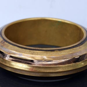 May include: A gold-toned bangle bracelet with a ridged design and a dark brown band.