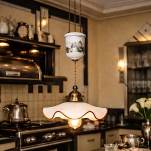 May include: A vintage-style hanging light fixture with a white, scalloped shade and a brass-colored base. The fixture has a decorative ceramic top with a painted landscape scene. The light is suspended by twisted cords, creating a warm, inviting ambiance in a kitchen setting.