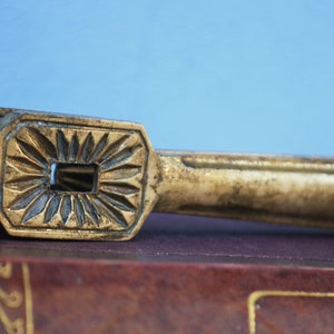 Pode incluir: Um quebra-nozes vintage de latão com um design decorativo em forma de estrela. O quebra-nozes está sobre um livro castanho.