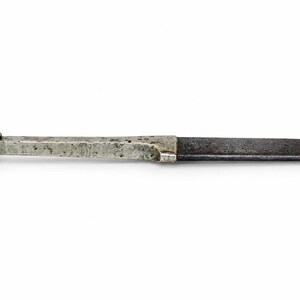 Könnte beinhalten: Ein verwittertes Klappmesser aus Metall mit einer dunklen, oxidierten Klinge und einem rechteckigen Griff. Der Griff verfügt über eine kleine, abgerundete Öse am Ende zum Aufhängen. Die Metalloberflächen weisen Altersspuren, Verfärbungen und Textur auf.