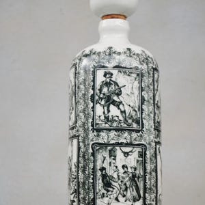 Może przedstawiać: Biała ceramiczna butelka z czarno-białym wzorem. Butelka ma unikalny, zaokrąglony korek i przedstawia wiele scen z ludźmi w tradycyjnych strojach.