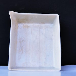May include: A white ceramic rectangular tray with a slightly curved edge. The tray has a smooth, glossy finish and appears to be used.