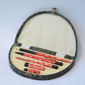 Puede incluir: Un juego de cuatro bolígrafos rojos y negros en una caja ovalada con estampado negro y blanco.