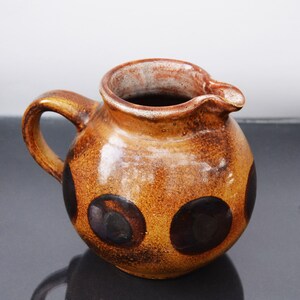 May include: A brown ceramic pitcher with a speckled glaze and dark brown polka dots. The pitcher has a rounded body and a handle.