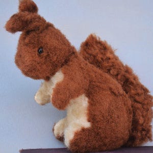 May include: A brown and white plush squirrel toy with a fluffy tail. The squirrel has a black button nose and black eyes.