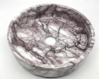 May include: A round, white marble sink with purple veining. The sink has a single drain hole in the centre.