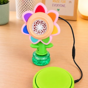 May include: A flower-shaped bubble machine with multicoloured petals and a green stem base, connected by a black cord to a round, lime green push-button switch. The bubble blower features a central white fan mechanism for creating bubbles.