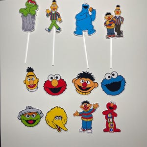 May include: A set of 11 Sesame Street character cake toppers. The toppers feature Elmo, Big Bird, Cookie Monster, Oscar the Grouch, Bert and Ernie, and more. The toppers are printed on cardstock and attached to wooden dowels.