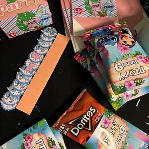 May include: A collection of party favors featuring a blue cartoon character with large ears. The favors include small boxes, bags, and cupcake toppers. The boxes and bags are decorated with a tropical theme and the text "Party Turns 9". The cupcake toppers are blue and white with the same cartoon character.