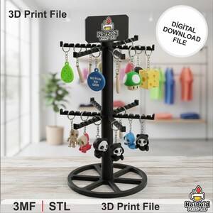 May include: A black display stand showcasing various keychains with diverse designs, including a mushroom, cheese, and panda figures. The stand has a circular base and multiple tiers. Text on the stand reads "3D Print File" and "Digital Download File".