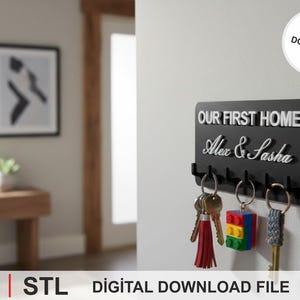 May include: A black key holder with the text "OUR FIRST HOME" and the names "Alex & Sasha" in white. The key holder has six hooks with keys hanging from them. A digital download file.