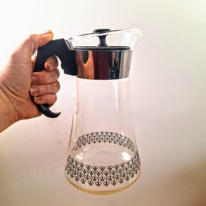 May include: A clear glass jug with a black handle and lid. The jug has a black and white geometric pattern around the bottom.