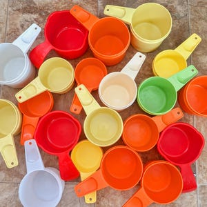 May include: A collection of colorful measuring cups in various sizes and shades, including white, red, orange, yellow, and green. The cups are made of plastic and have handles for easy use. Ideal for baking and cooking.