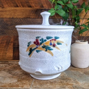 May include: White ceramic lidded jar with a crackled glaze and a floral design in shades of yellow, green, red, and blue.