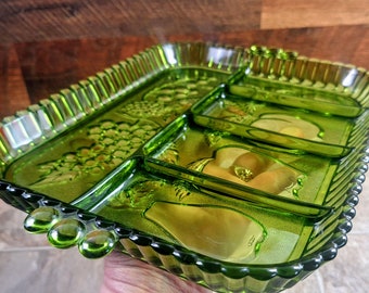 May include: A green glass serving tray with four divided sections. The tray has a raised, textured rim and a design of fruit, including grapes, pears, and apples.