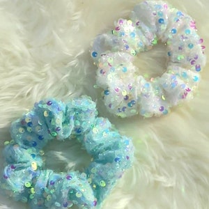 Peut inclure: Deux chouchous avec des paillettes irisées. L'un est blanc et l'autre est bleu clair.