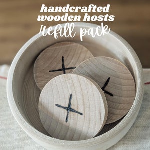 May include: A wooden bowl filled with four wooden game pieces. Each piece has a black cross drawn on it. The bowl and pieces are light brown in color. The text "handcrafted wooden hosts refill pack" is written in white letters on a brown background.