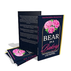 May include: A stack of books with the title "Bear in a Bakery" and a floral design. The cover features pink flowers and the author's name, Liz Paffel. The book is part of the "Estes Park Shifters" series.