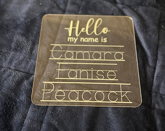 May include: A clear acrylic dry-erase board with the text "Hello my name is" and three lines with dotted lines for writing the names "Camara", "Fanise", and "Peacock".