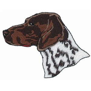 Może przedstawiać: Haftowana naszywka przedstawiająca profil głowy psa. Pies ma brązowe futro na głowie i uszach oraz biało-czarny wzorzysty kark. Naszywka jest przeznaczona do przyszywania lub naprasowywania na odzież lub tkaninę.