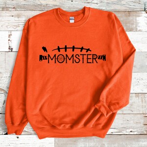 May include: Orange sweatshirt with a black graphic of stitches and the text "MOMSTER".