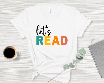May include: White t-shirt with the text "let's READ" in black, with the word "READ" in colorful block letters: teal, yellow, and orange.