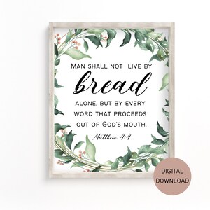 Op de afbeelding: Een printbaar wanddecoratiedesign met een groene krans van bladeren en de quote "De mens zal niet van brood alleen leven, maar van elk woord dat uit de mond van God voortkomt. Mattheüs 4:4".