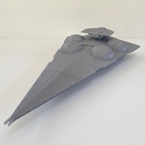 Puede incluir: Maqueta gris en forma de triángulo de una nave espacial, con cuatro estructuras en forma de cúpula y un puente rectangular. El modelo tiene un frente largo y puntiagudo, sobre fondo blanco. Réplica detallada.