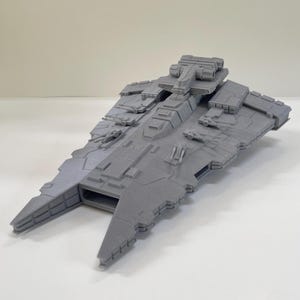 Puede incluir: Modelo gris de una nave espacial con detalles intrincados, incluyendo múltiples torretas, paneles y una sección de mando central. El modelo tiene un diseño elegante y angular, con dos secciones frontales extendidas. Es un objeto de colección.